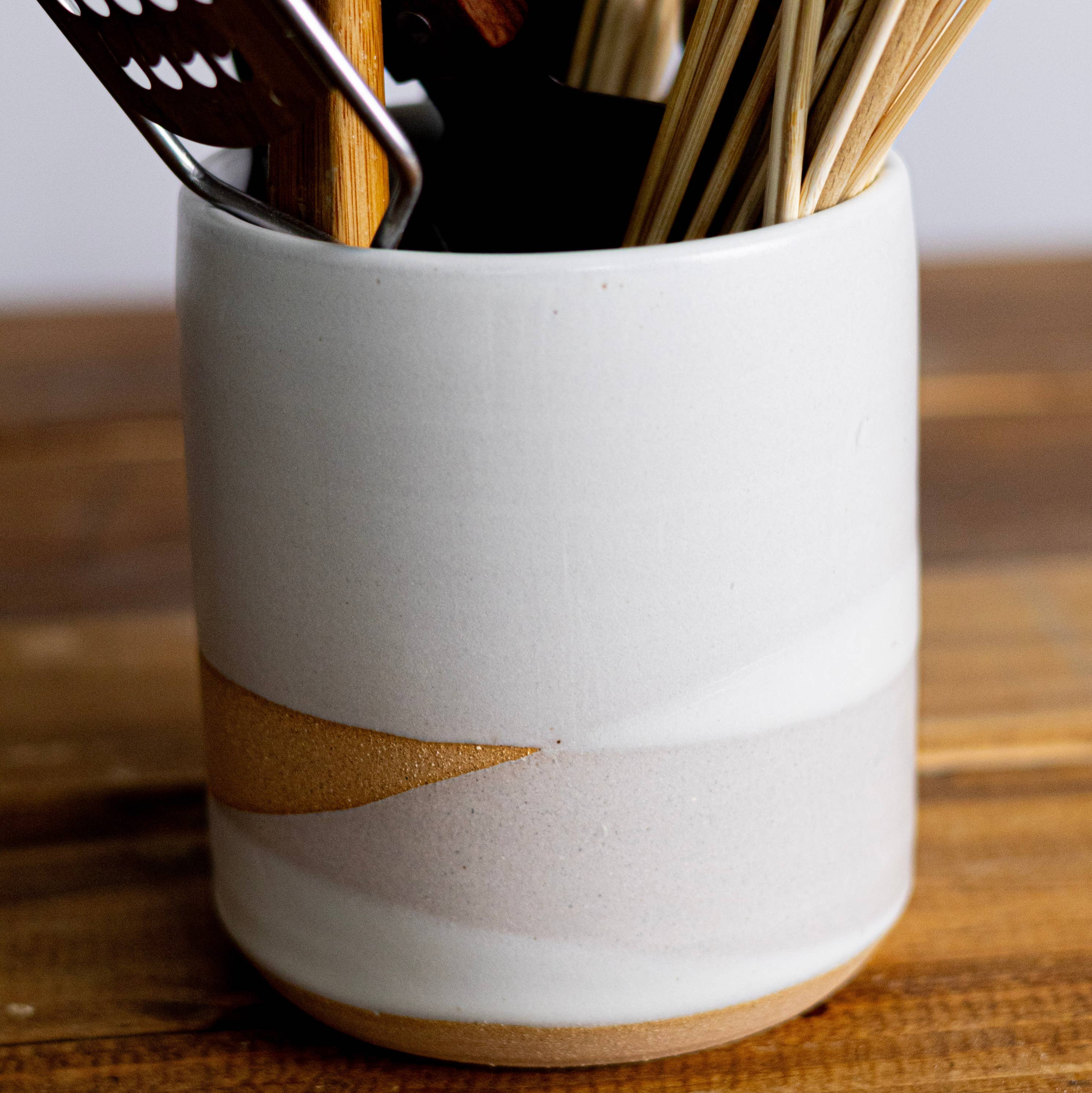 Ceramic utensil holder with kitchen utensils on a wooden surface