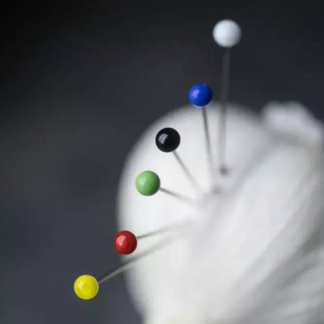 Close-up of a pin cushion with colorful pins on a dark background