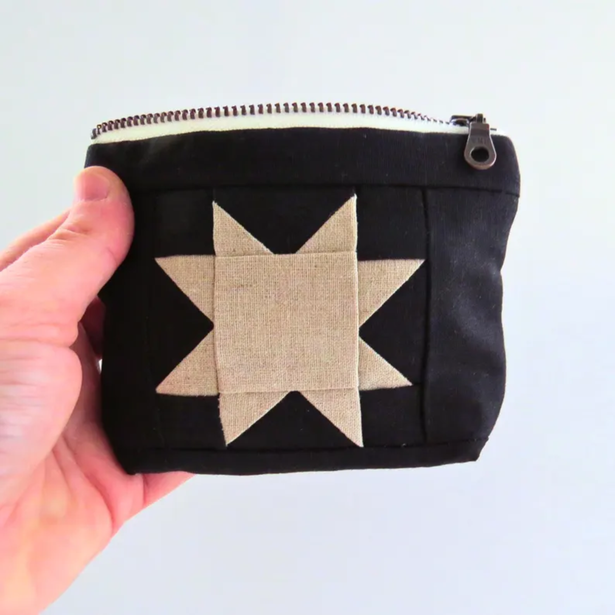 Black pouch with a beige star design held by a hand against a light background