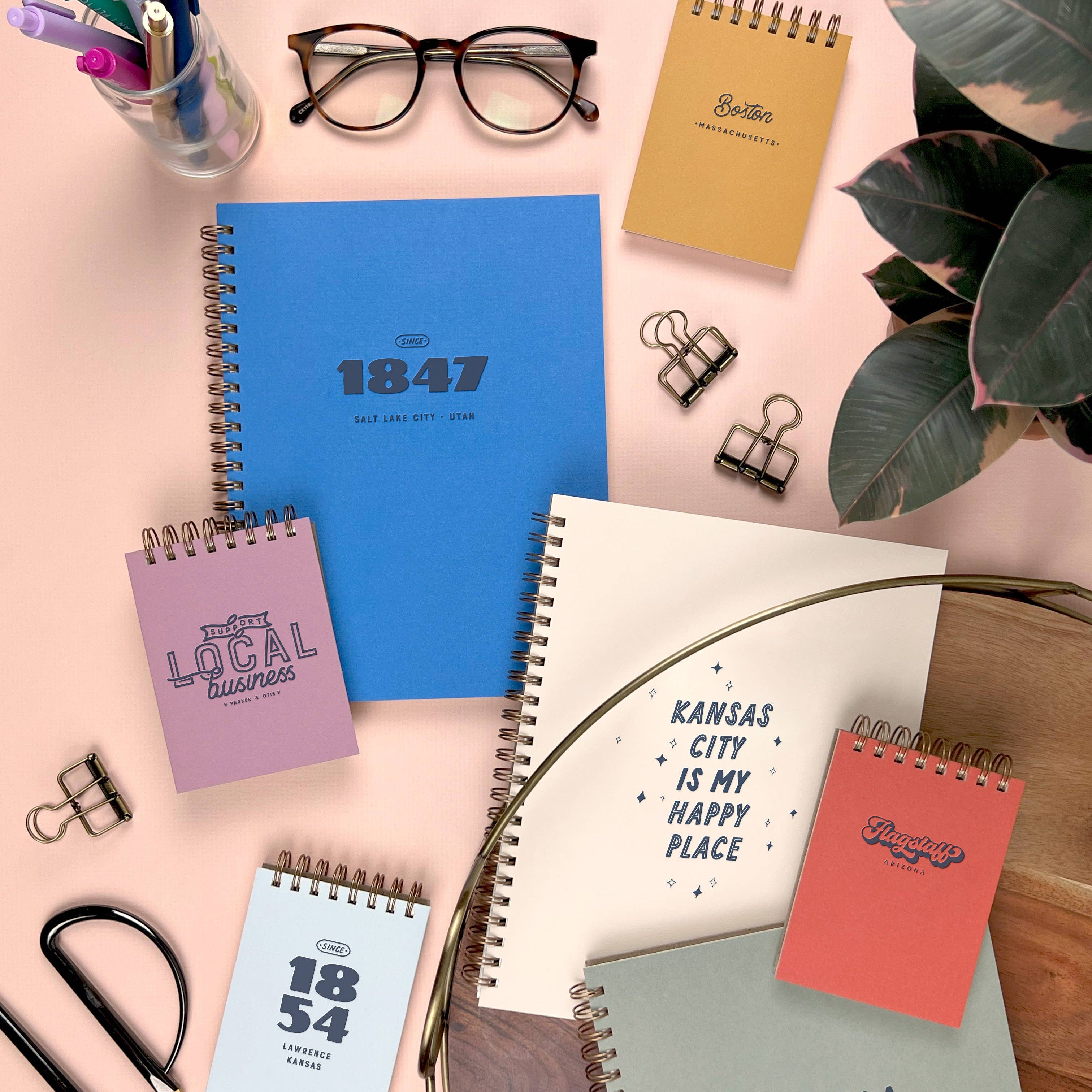 Collection of spiral-bound notebooks with various designs and text on a pink surface.