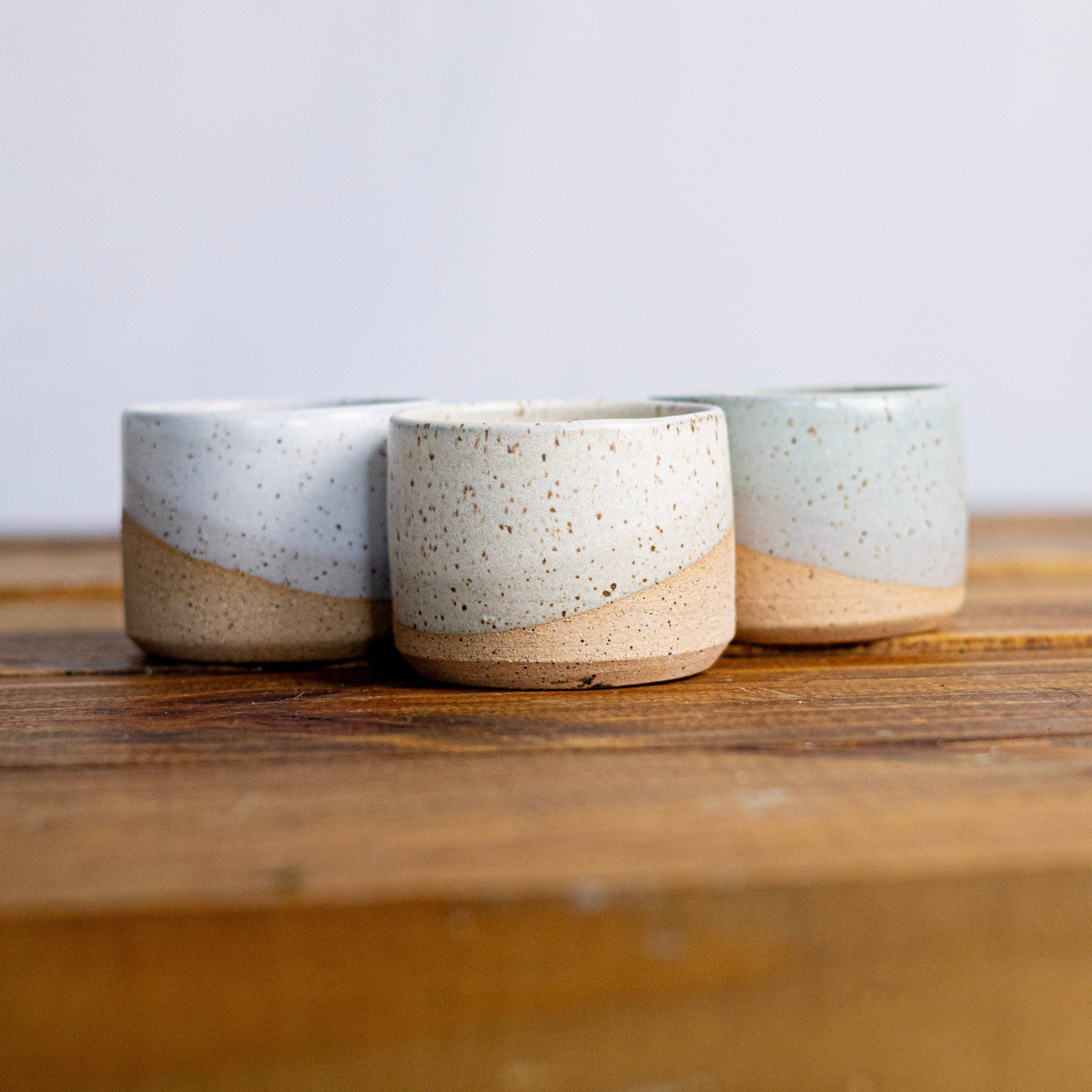 Three ceramic pots/cups with speckled glaze on a wooden surface