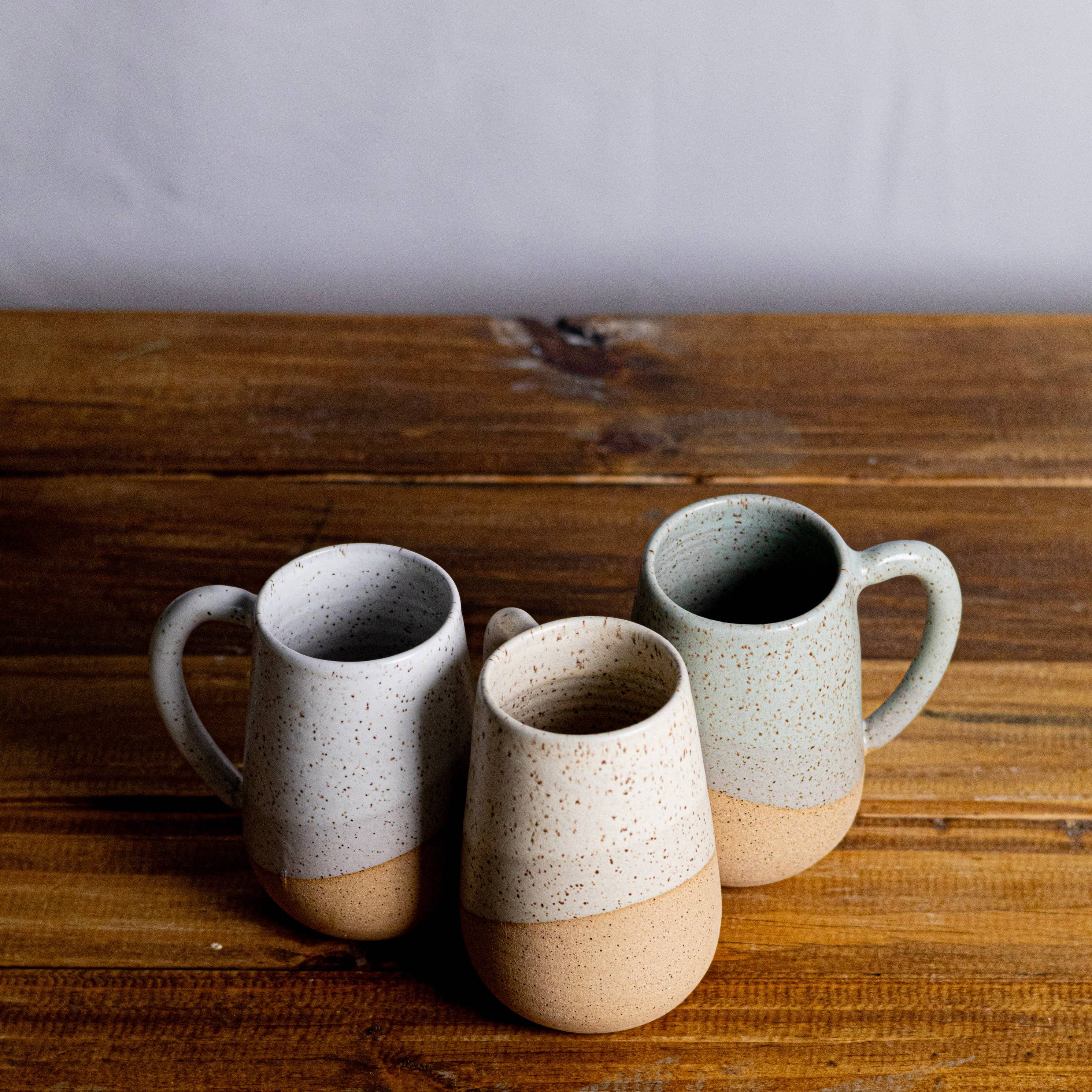 Three ceramic mugs with speckled glaze on a wooden surface