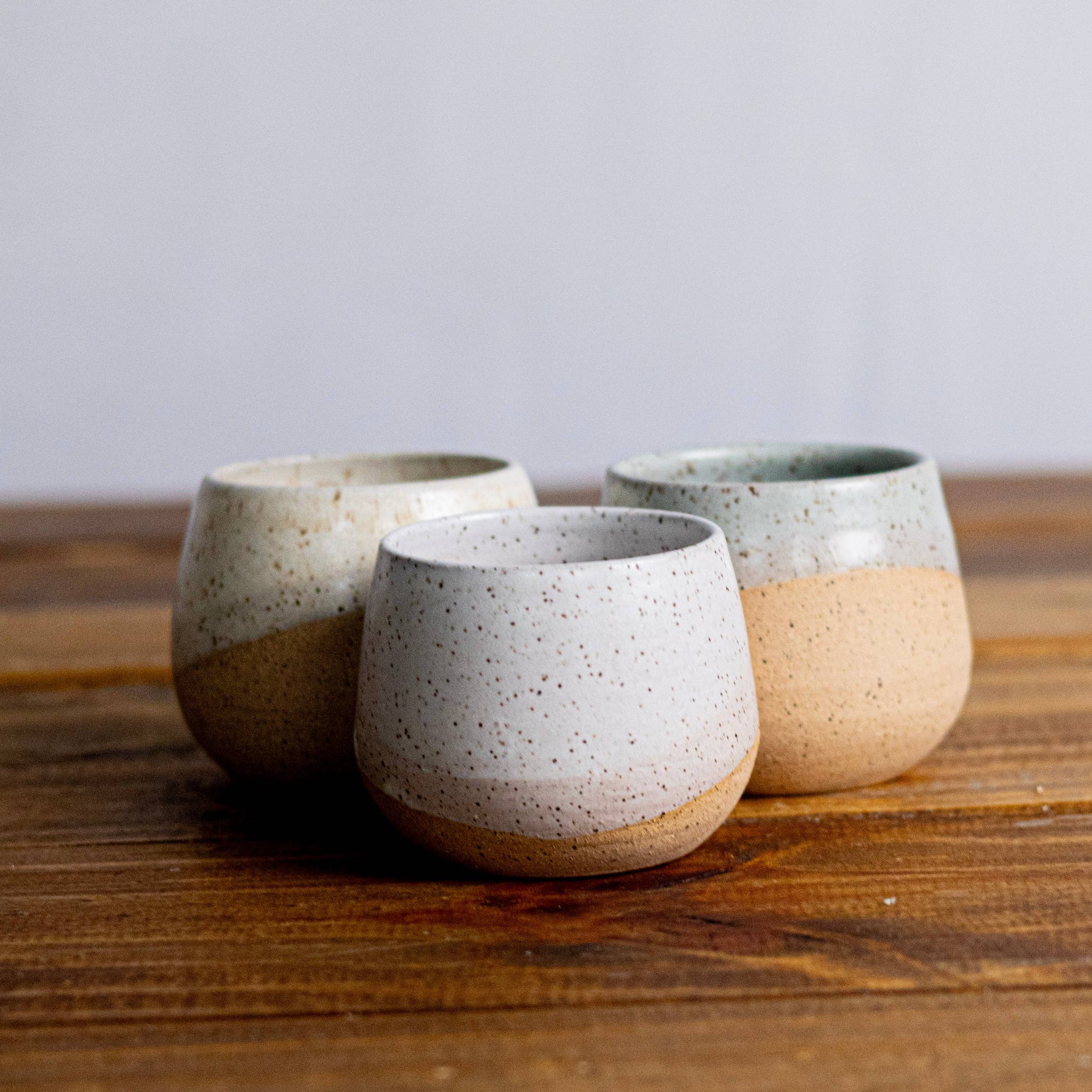 Three ceramic cups with speckled glaze on a wooden surface