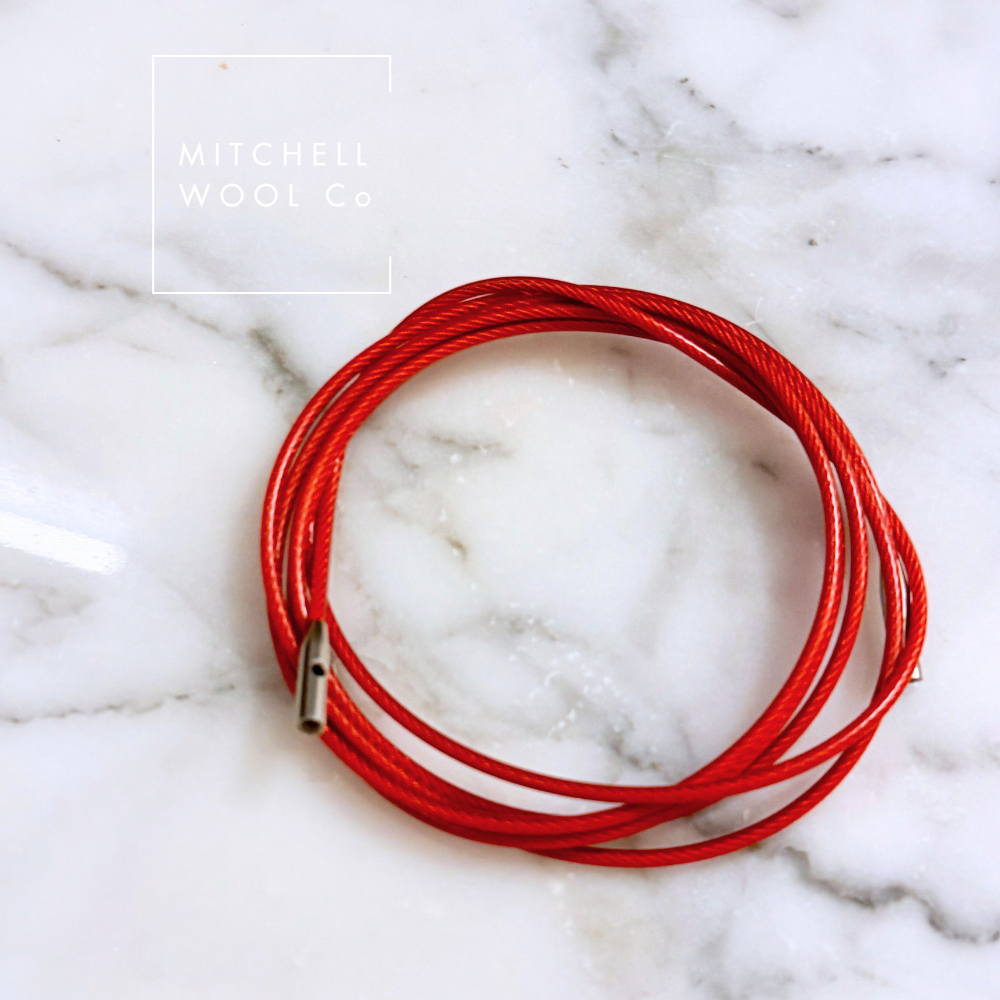 A coiled red cable  with a silver metal clasp, displayed on a white and gray marble surface. The brand name 'Mitchell Wool Co' is visible in the top left corner.