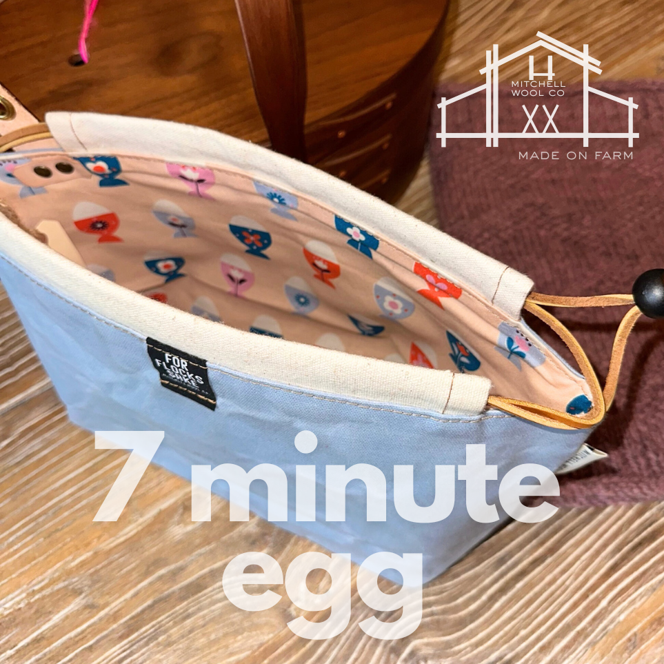 Waxed cotton project bag with scandinavian eggs on the interior and blue exterior on a wooden surface, Mitchell Wool Co logo visible.