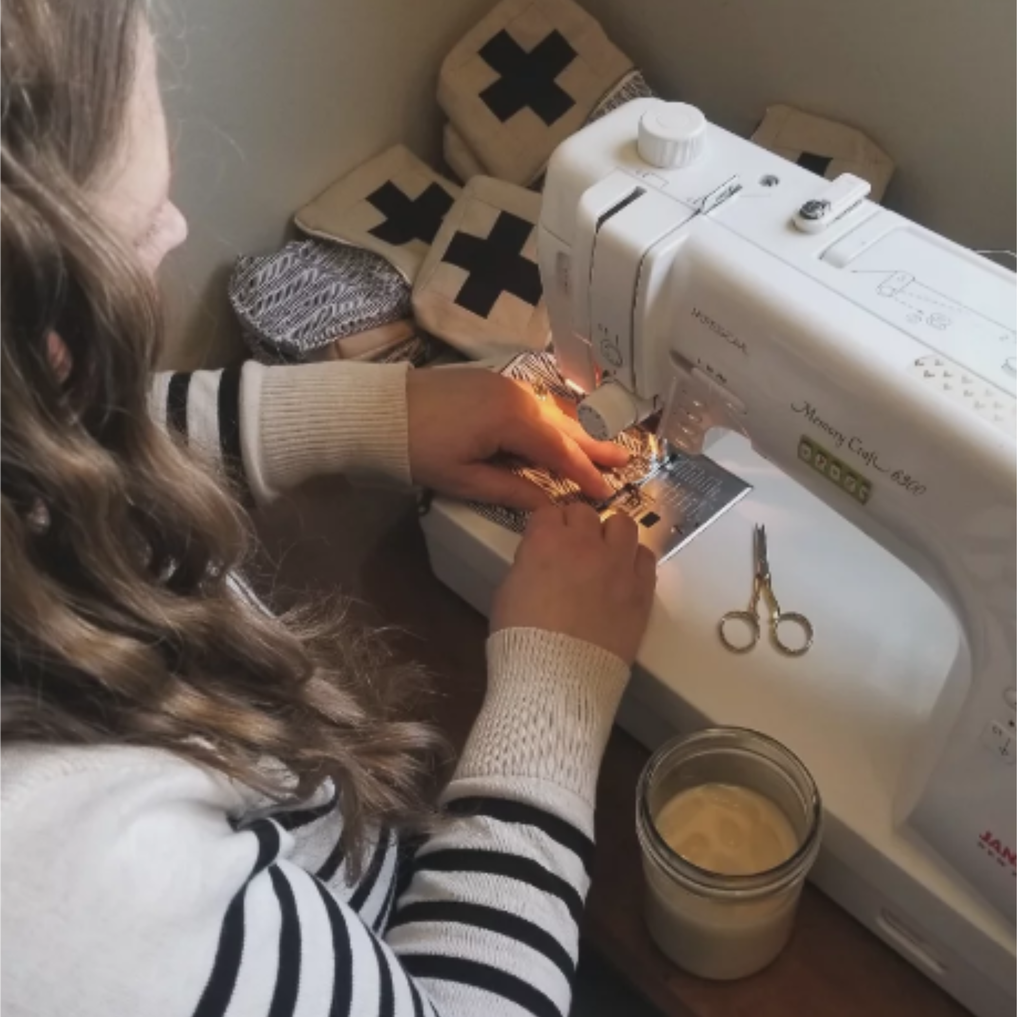 Person using a sewing machine with various items on a table