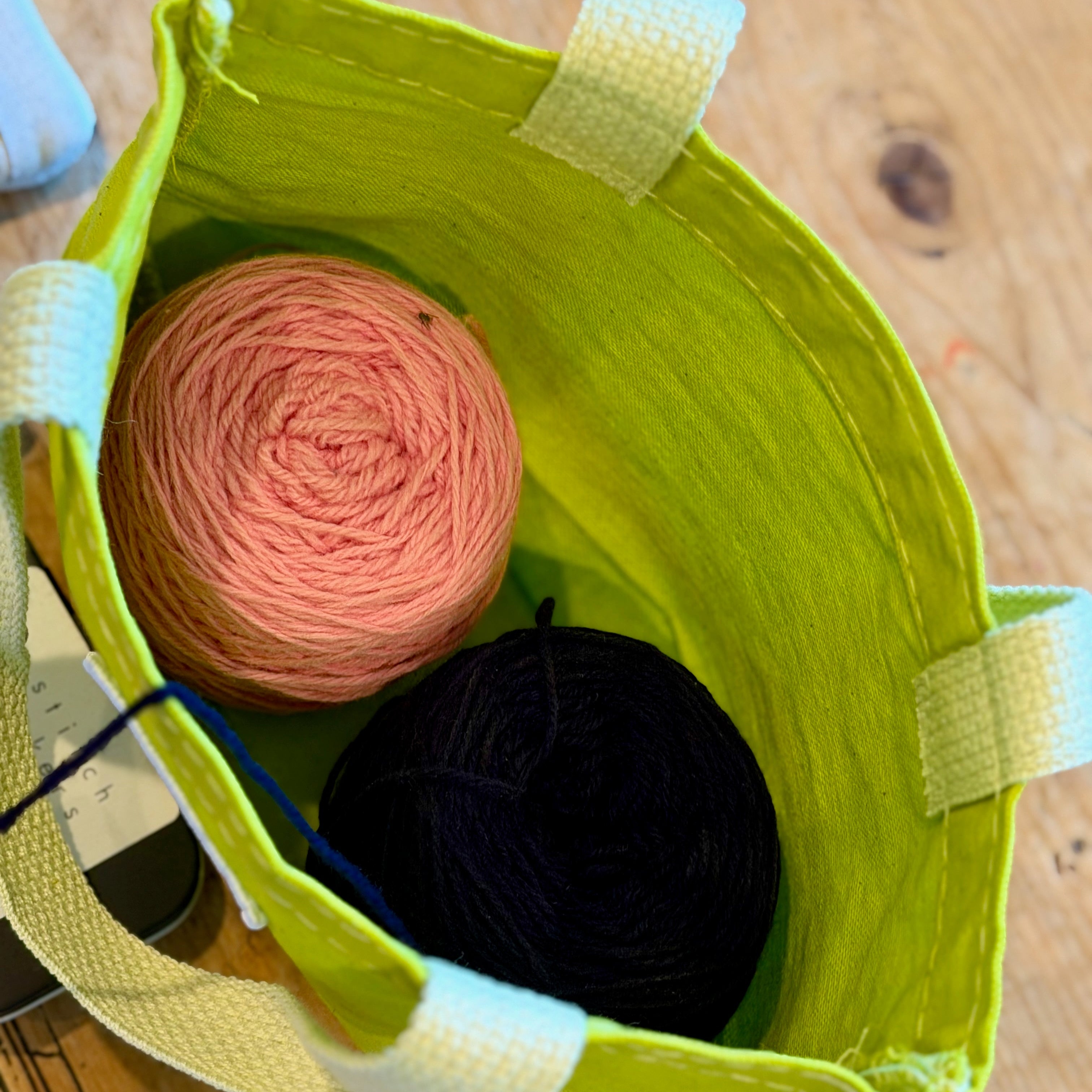 TOP VIEW OF CITRON BITTY yarn project bag with pink and midnight yarn on a wooden surface