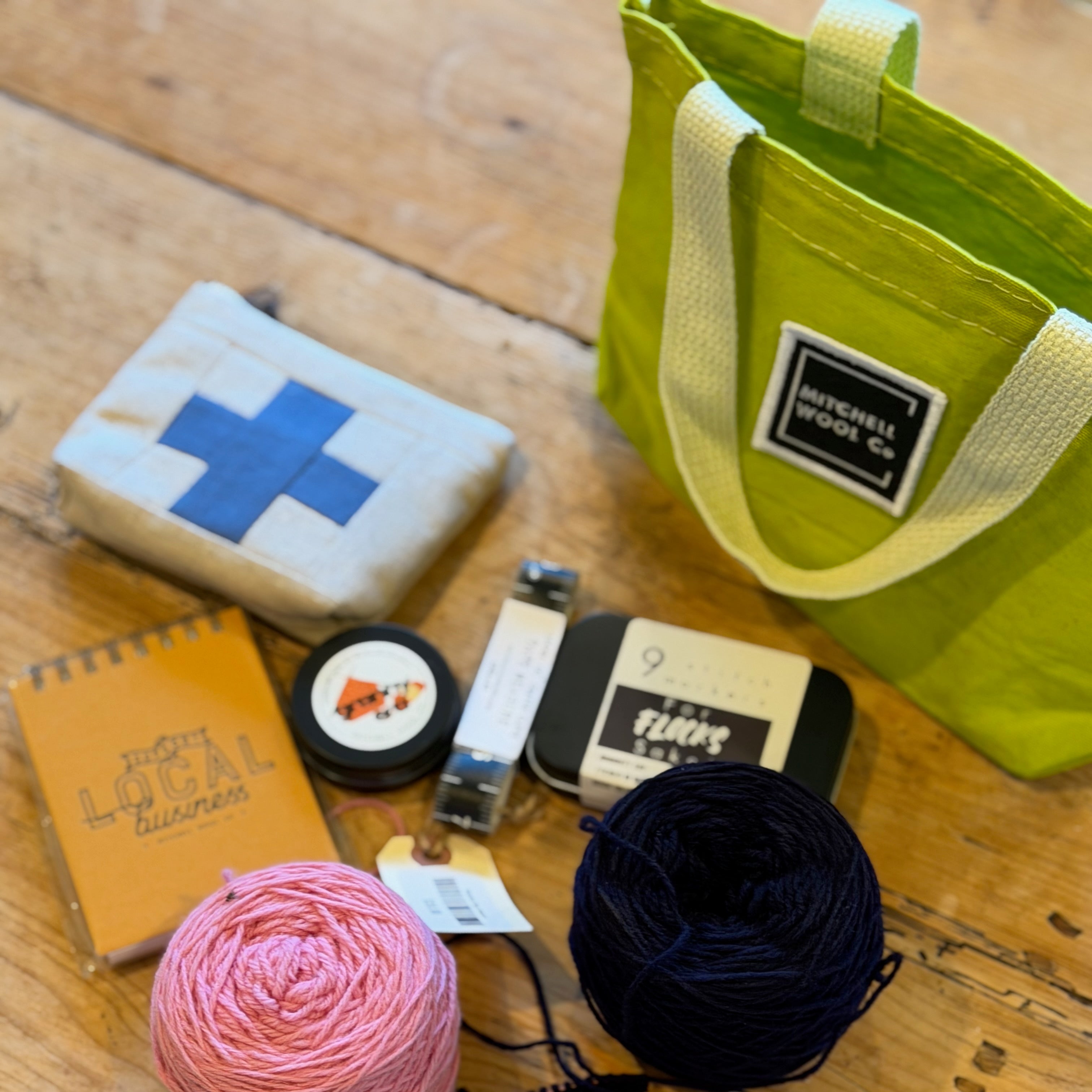 Showing what fits in the bitty bag - Yarn, knitting needles, and a green bag on a wooden surface
