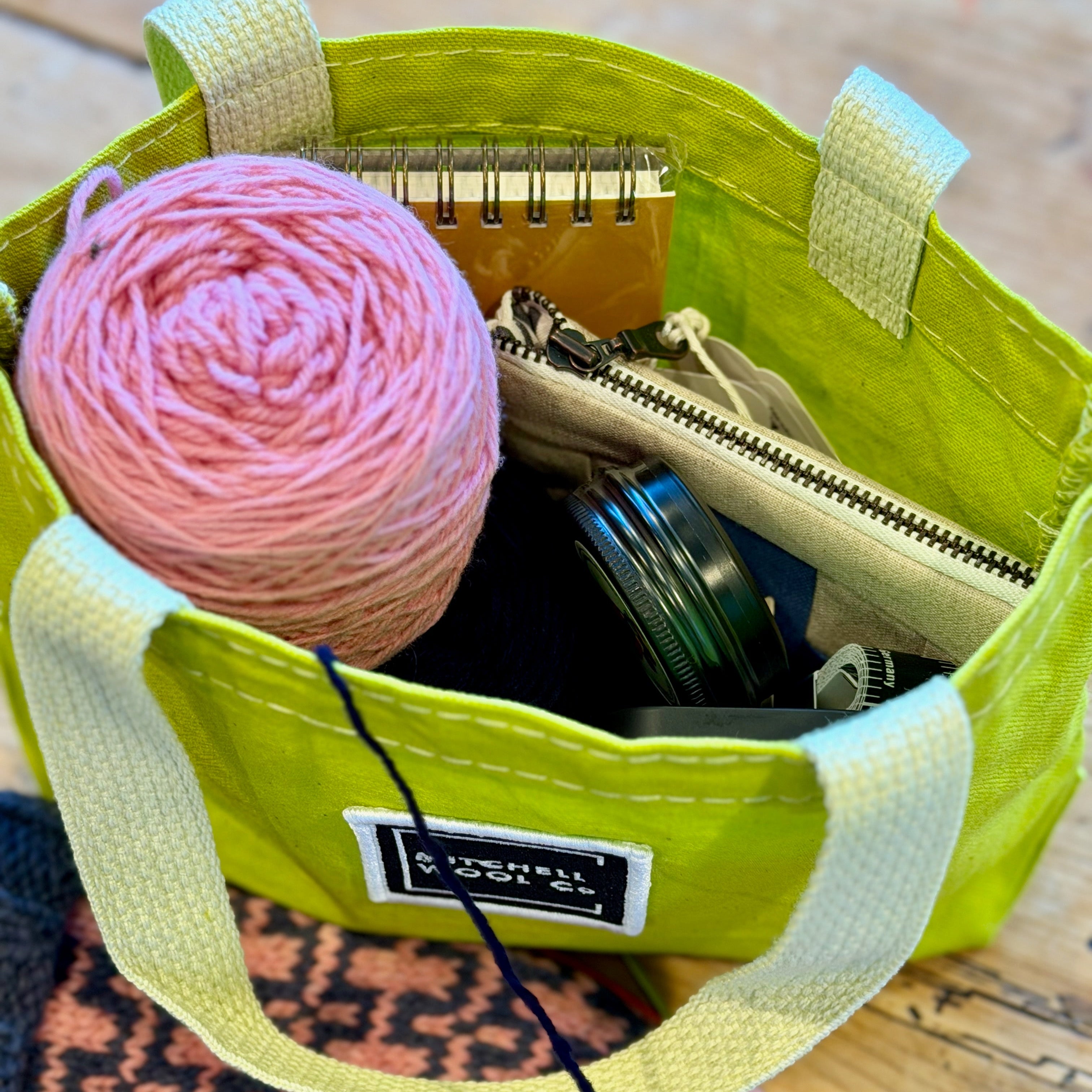Citron green bag with pink yarn and other items on a wooden surface