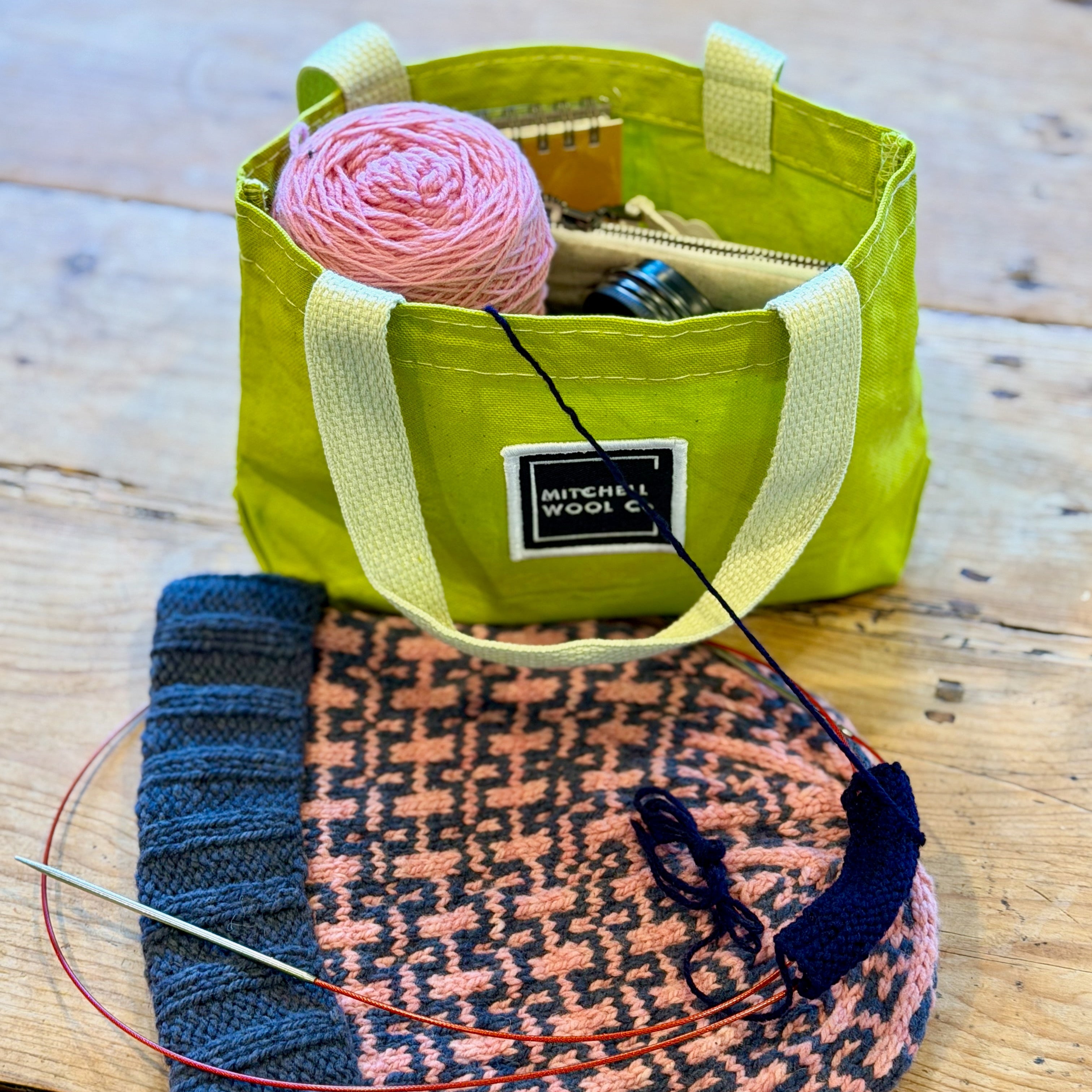 Green knitting bag with yarn and needles on a wooden table