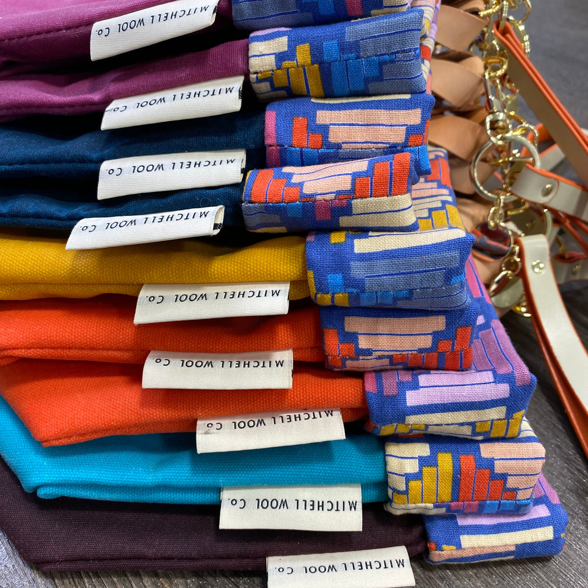 A stack of folded Mitchell Wool Co. fabric swatches in multiple colors, including purple, blue, teal, orange, and yellow, with one blue patterned swatch standing upright on the right.