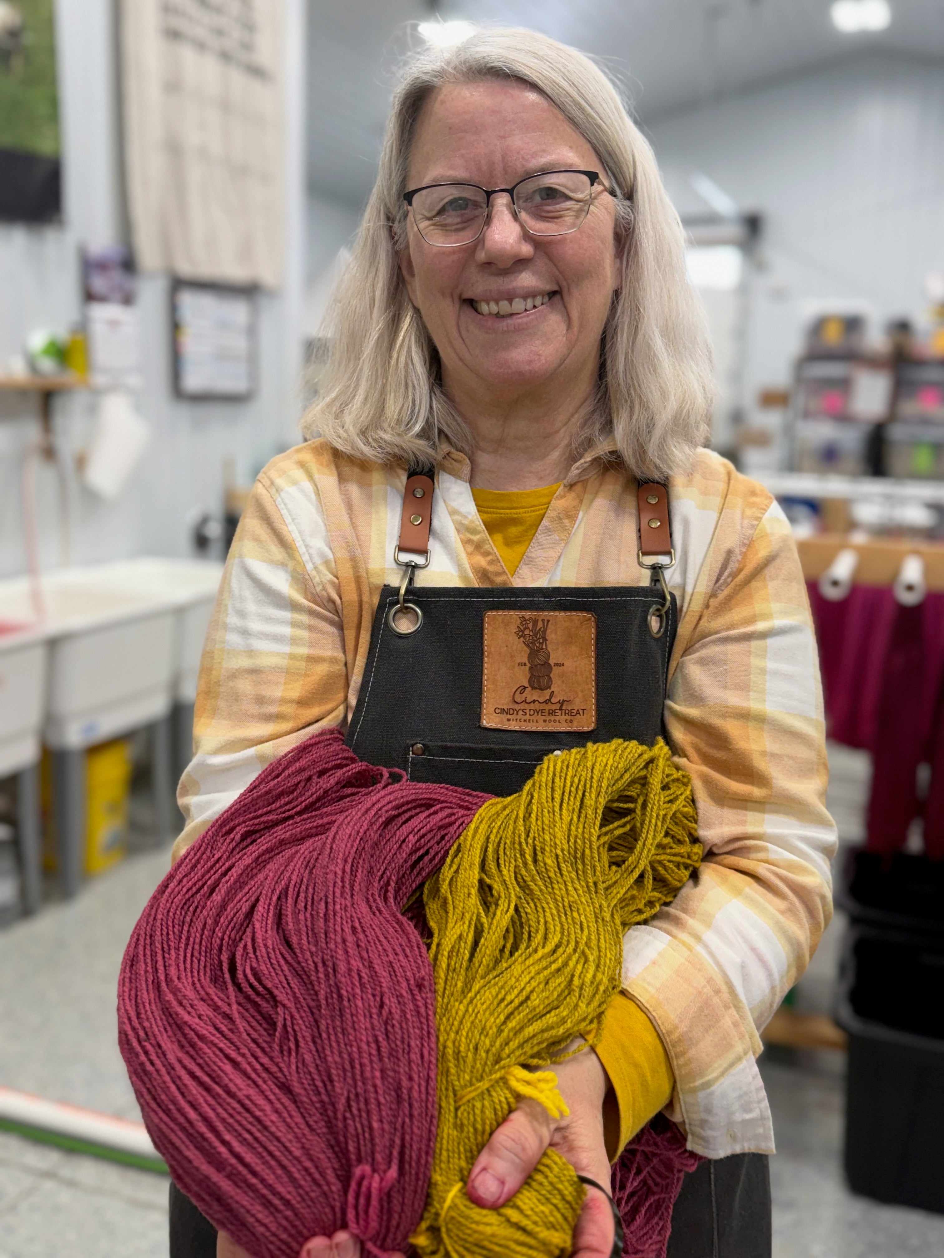 our Angel of Dyes! Cindy, the wizard behind all of these beautiful skeins holds the new colors for 2026 , GREATER GOOD (pink) and NEIGHBORS (gold) in our dye kitchen