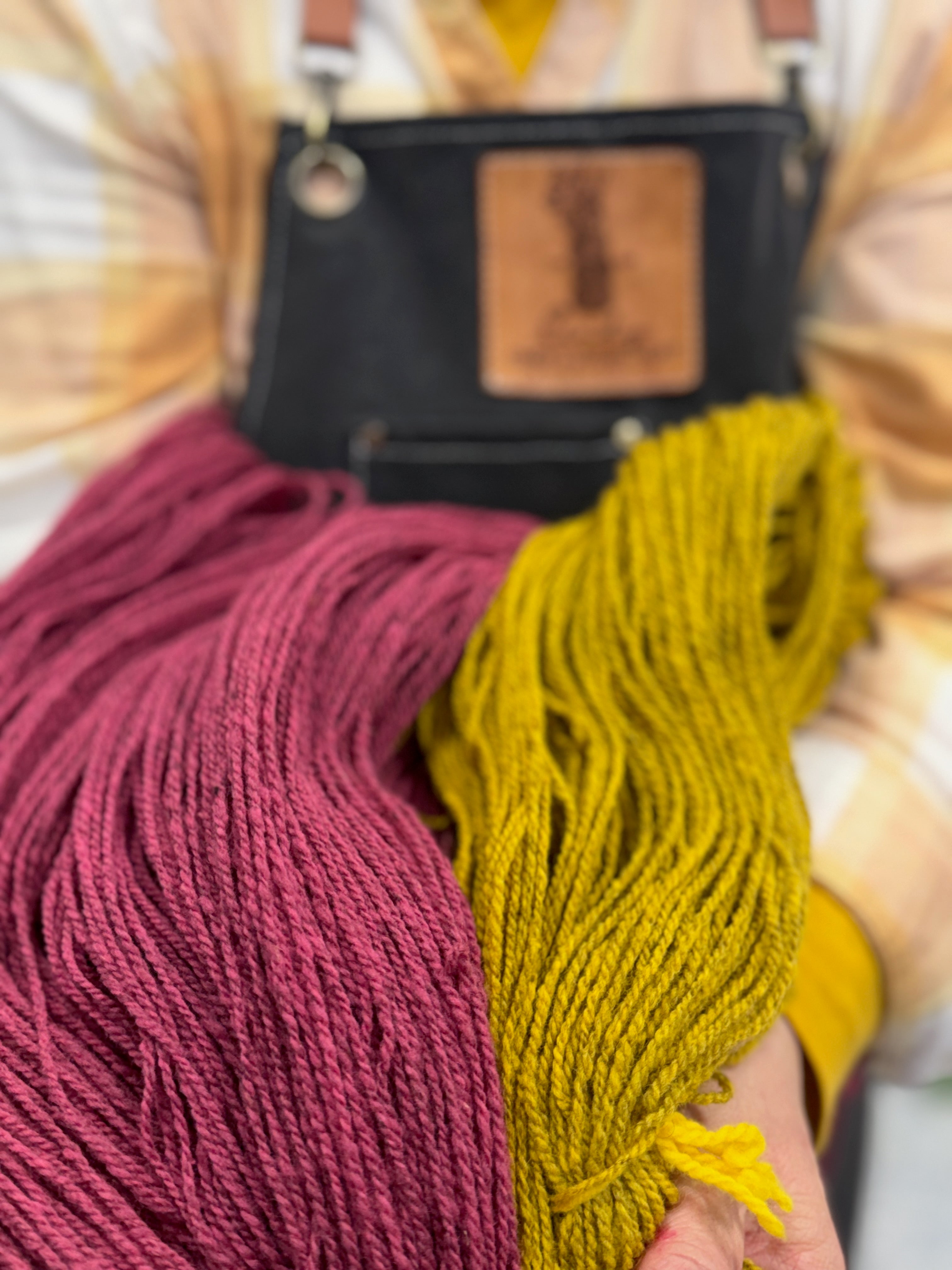 our Angel of Dyes! Cindy, the wizard behind all of these beautiful skeins holds the new colors for 2026 , GREATER GOOD (pink) and NEIGHBORS (gold) in our dye kitchen