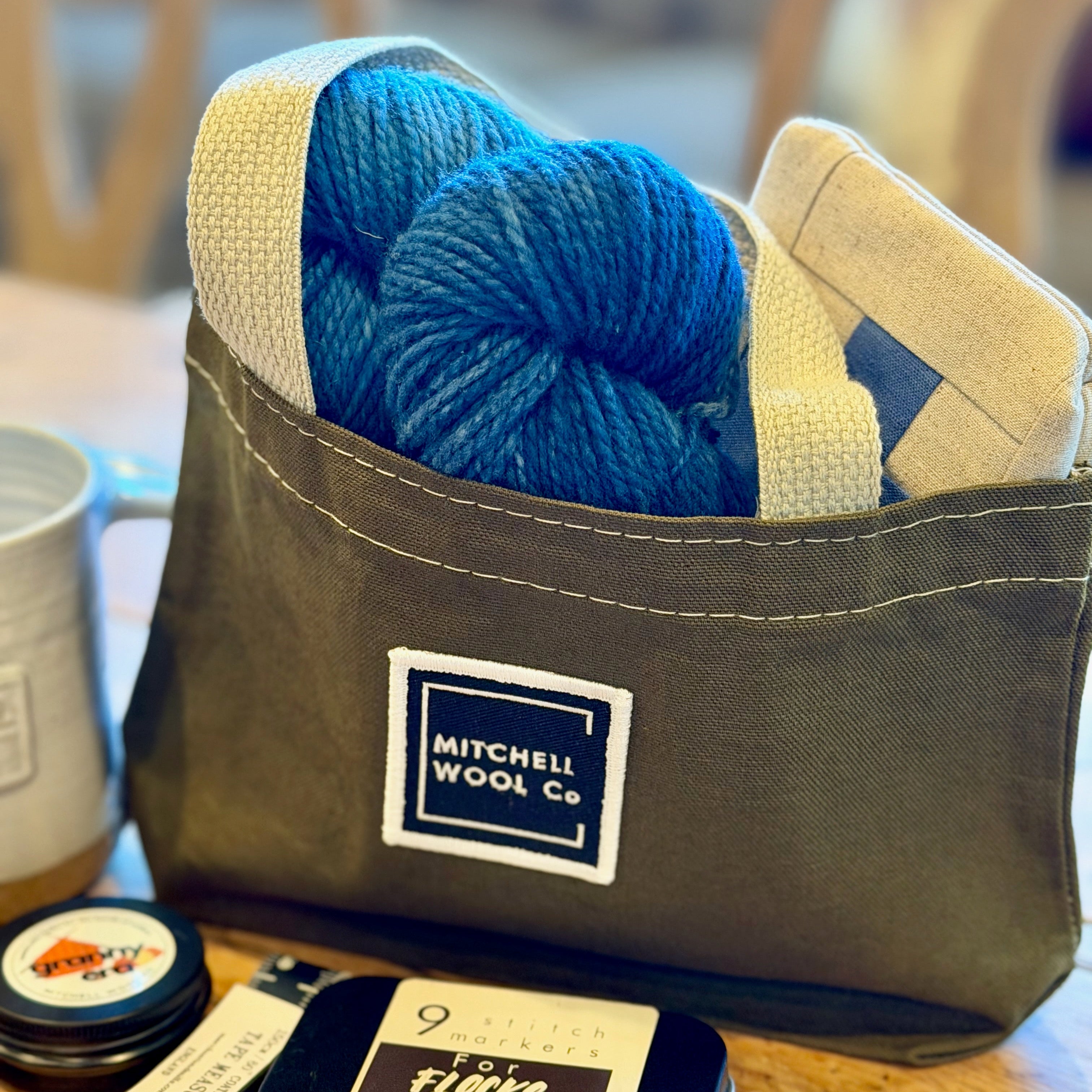 Olive bag with blue yarn and a label on a wooden table