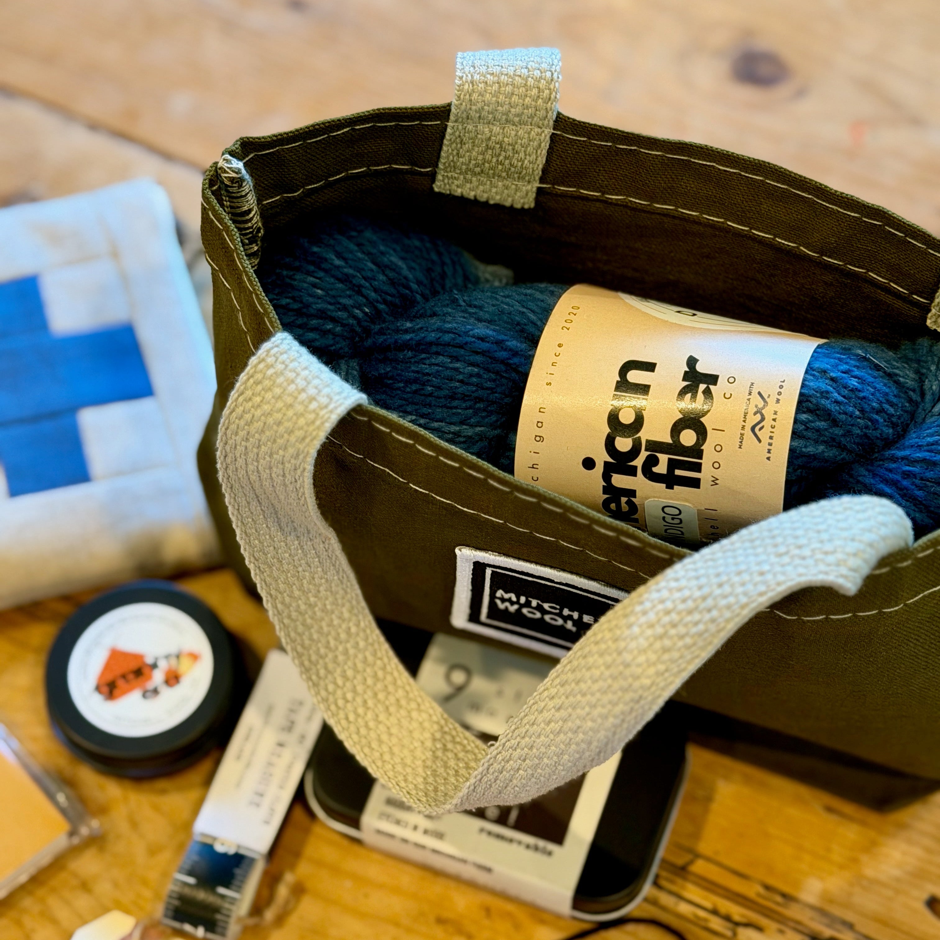 Olive project bag with yarn and notions on a wooden surface