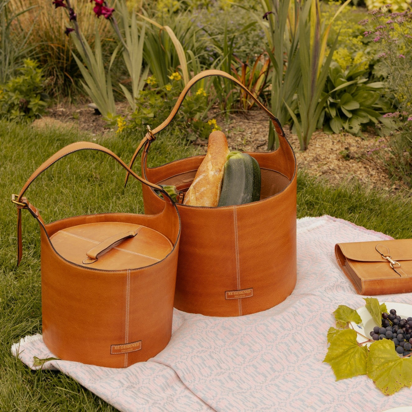 Two brown leather picnic baskets on a blanket with a garden background