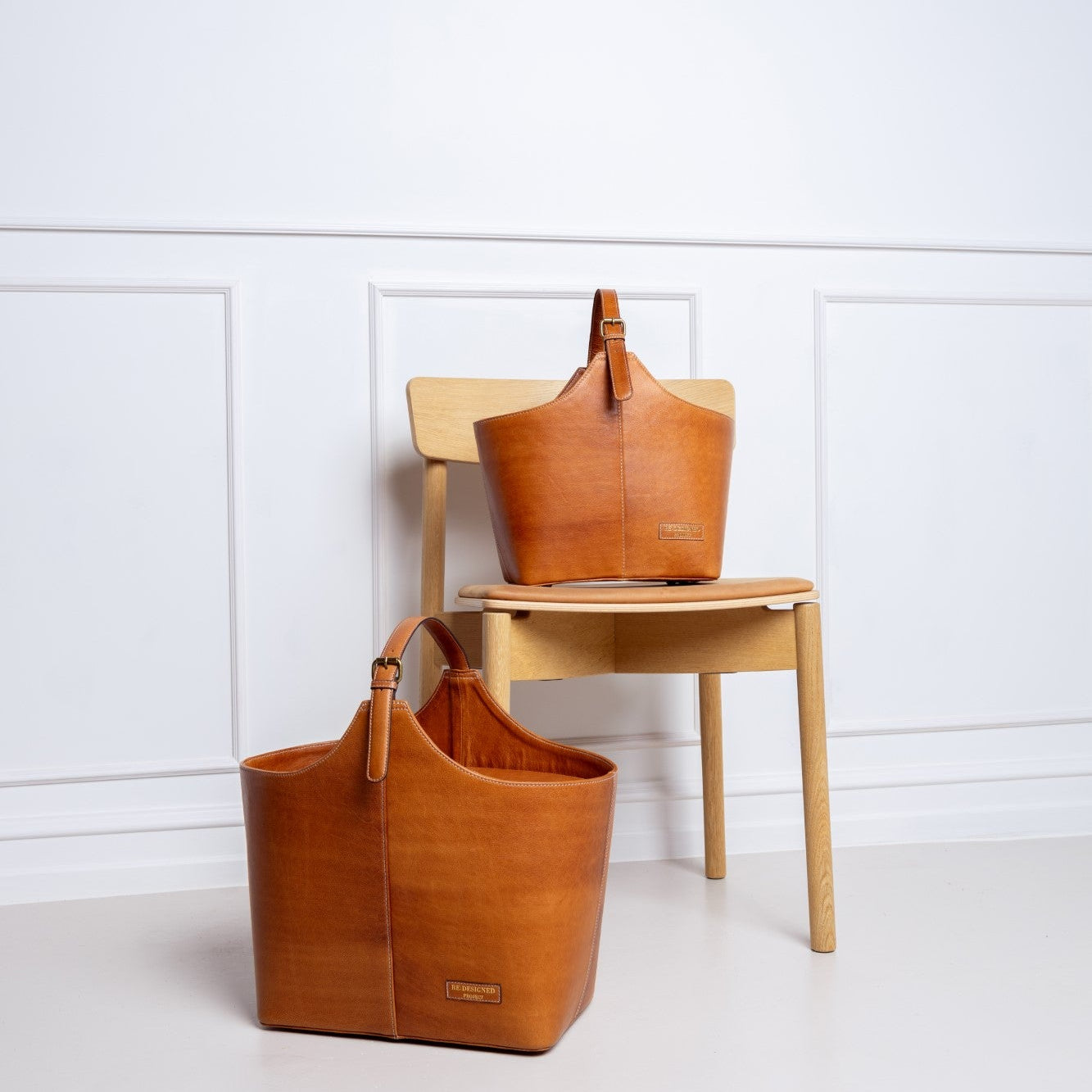 Two brown leather bags on a wooden chair against a white wall.