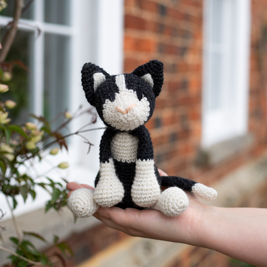Hand holding a black and white crochet cat toy with a blurred outdoor background
