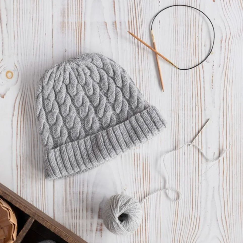 Gray knitted beanie with knitting needles and yarn on a wooden surface