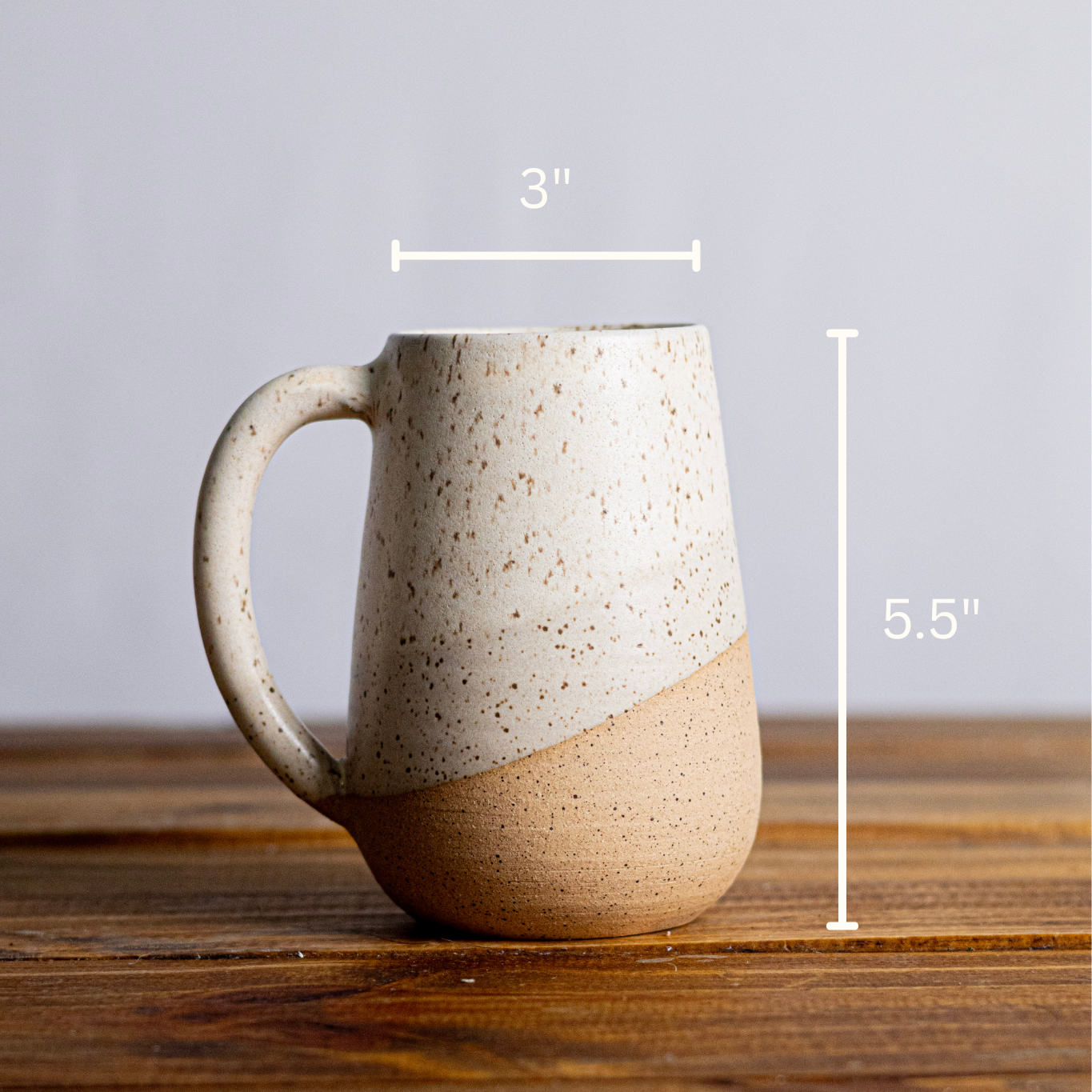 Speckled ceramic mug on a wooden surface with measurements indicated.
