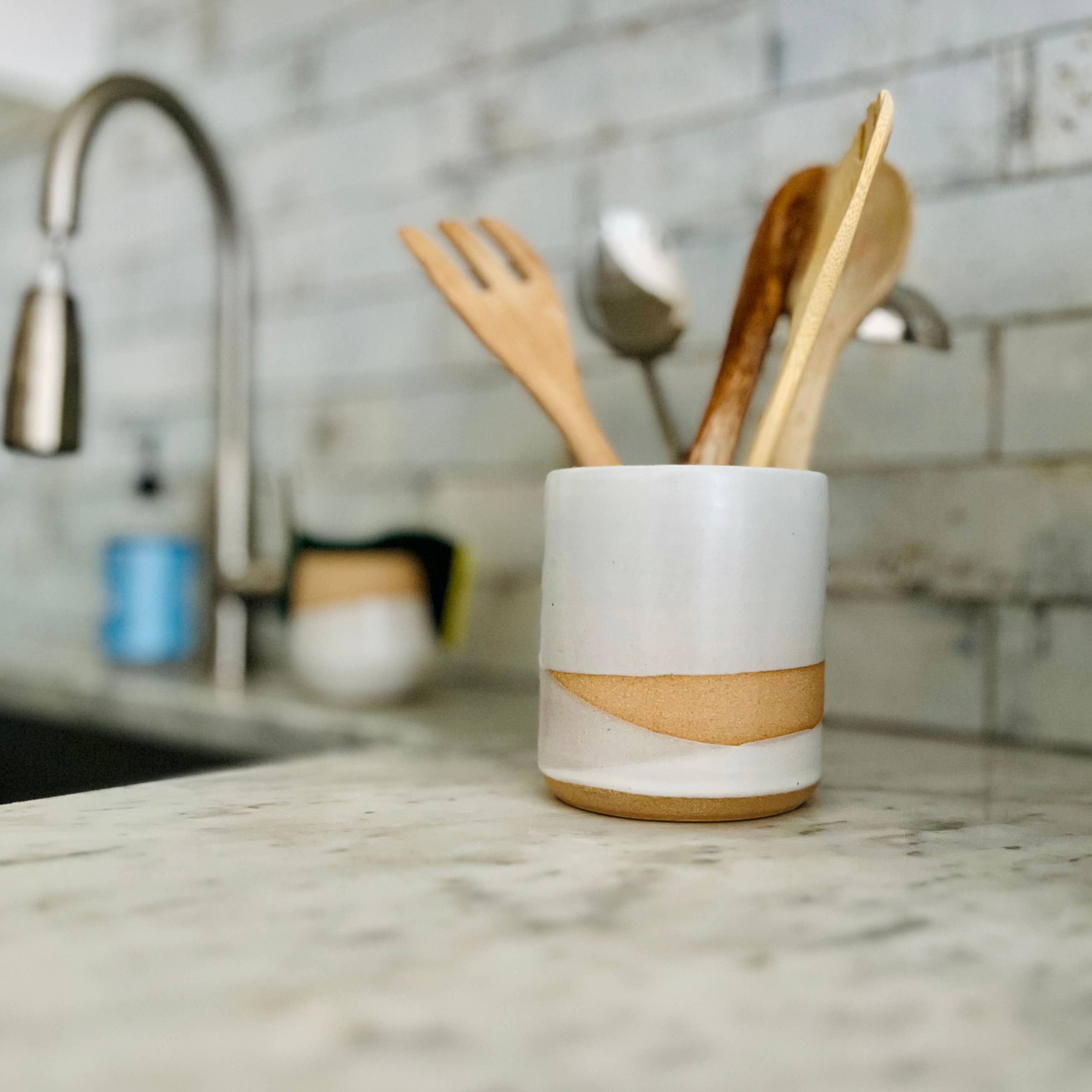 Ceramic utensil holder with wooden utensils on a kitchen counter