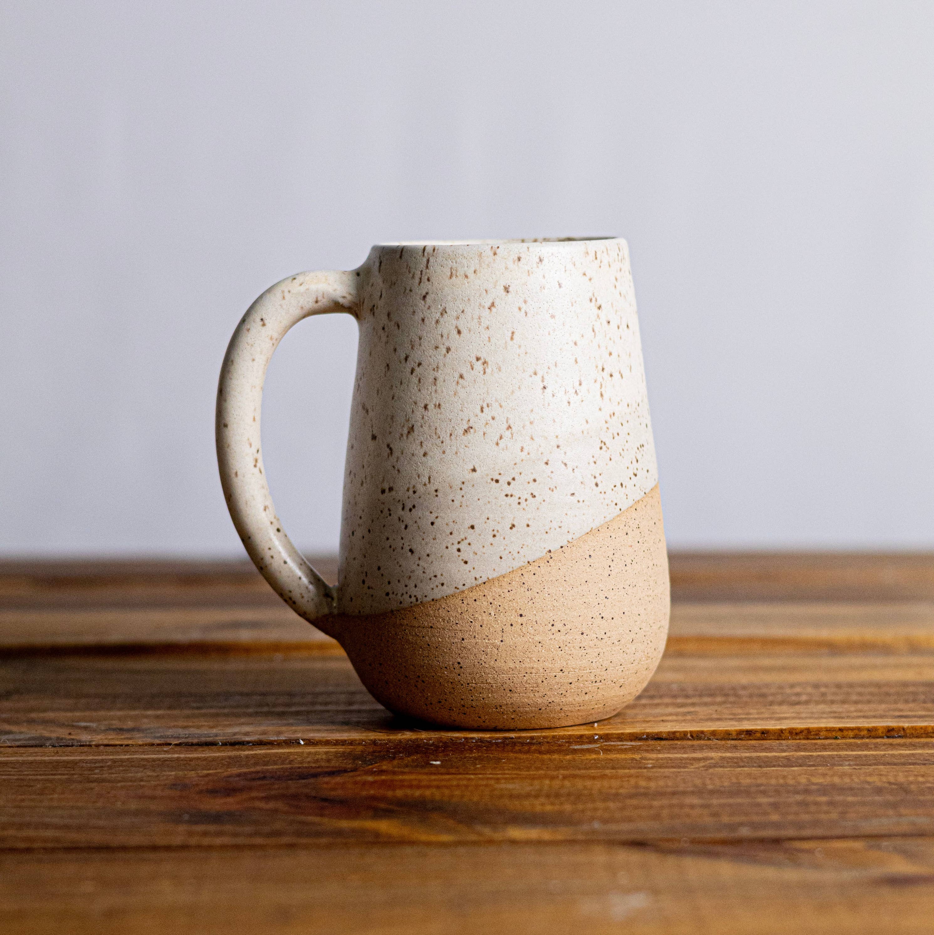 Speckled ceramic mug on a wooden surface with a plain background