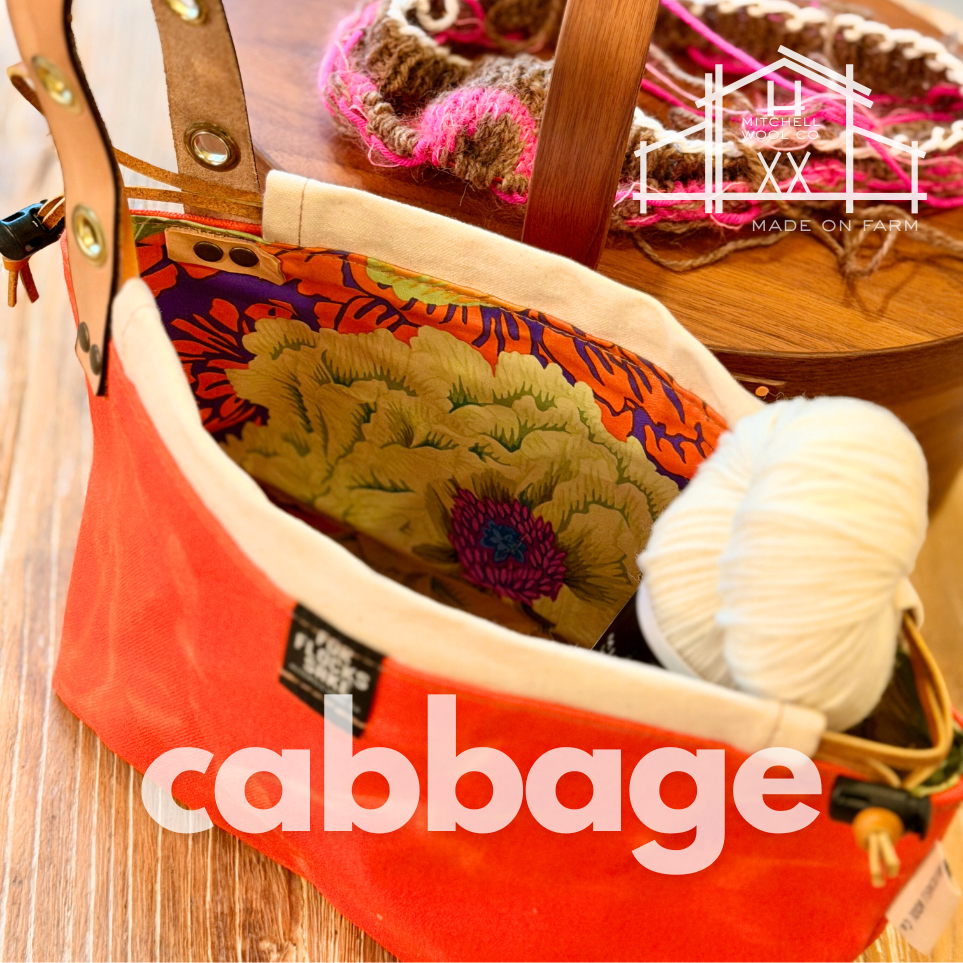 bright orange bag with floral design and yarn ball on a wooden surface, featuring 'cabbage' brand.