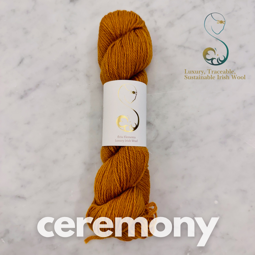 Squash yellowy Orange skein of yarn with a label on a marble background, featuring the brand 'Ceremony'.