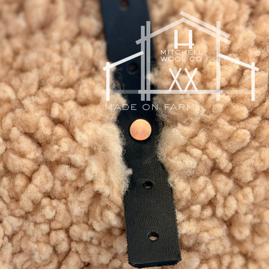 Black leather strap with a gold RIVET on a textured beige background, featuring Mitchell Wool Co branding. - OUR STRAPS ARE ADJUSTABLE TO BE SIZE INCLUSIVE AND OFFER A WIDE VARIETY OF CARRY OPTIONS