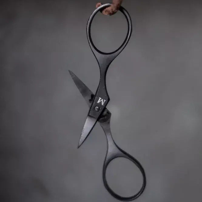 Pair of black-handled scissors hanging on a dark background