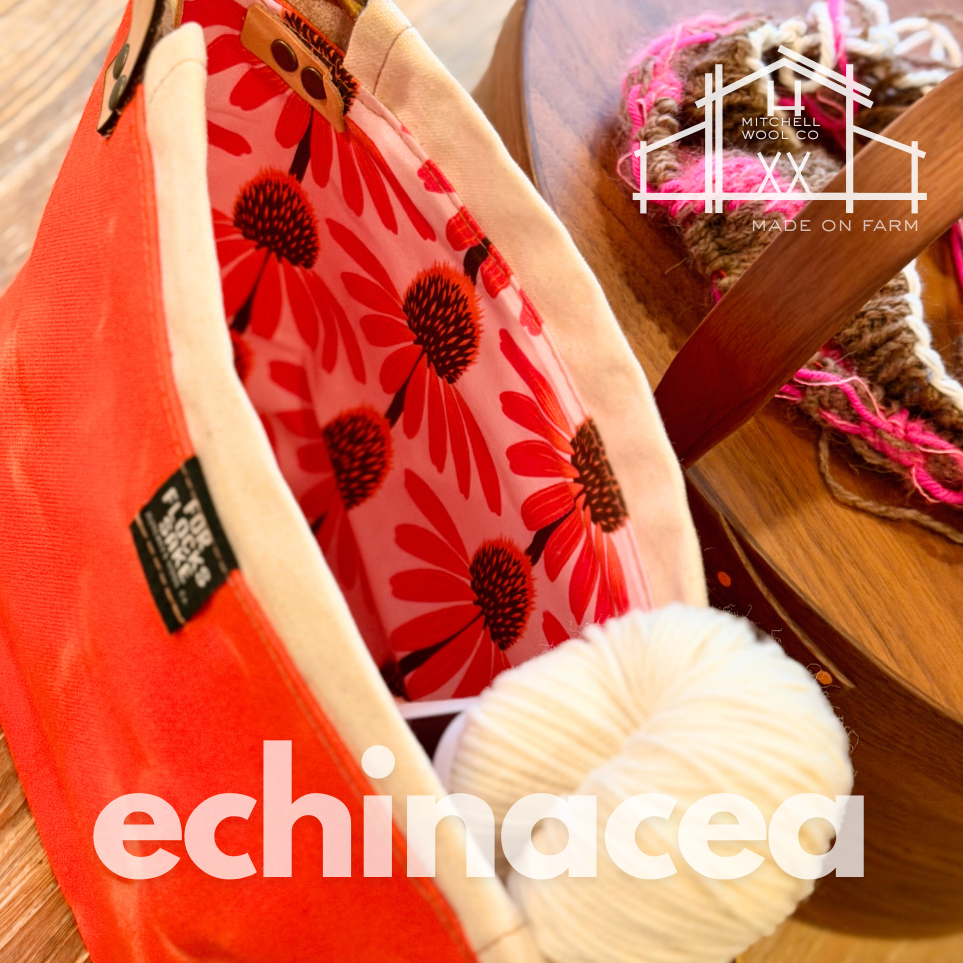 bright pink floral-patterned project bag with orange waxed'echinacea' text on a wooden surface, featuring Mitchell Wools branding.