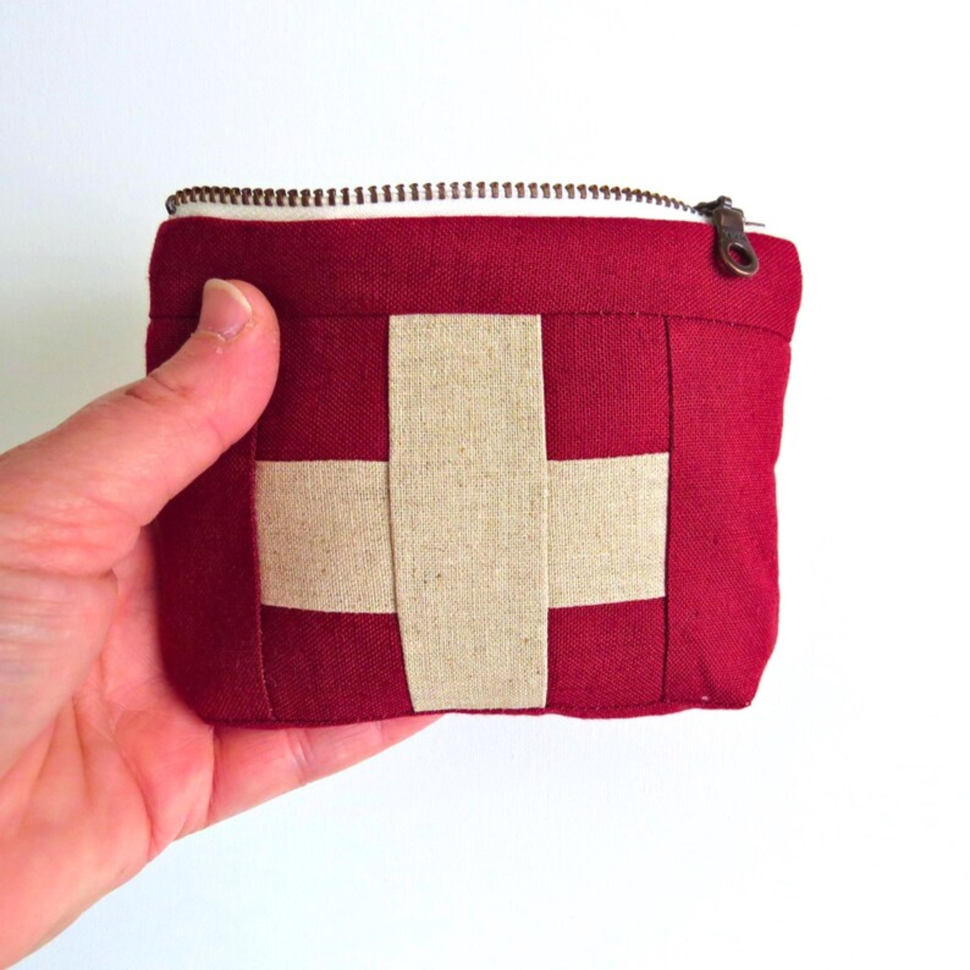 Red fabric pouch with beige square held by a hand on a white background