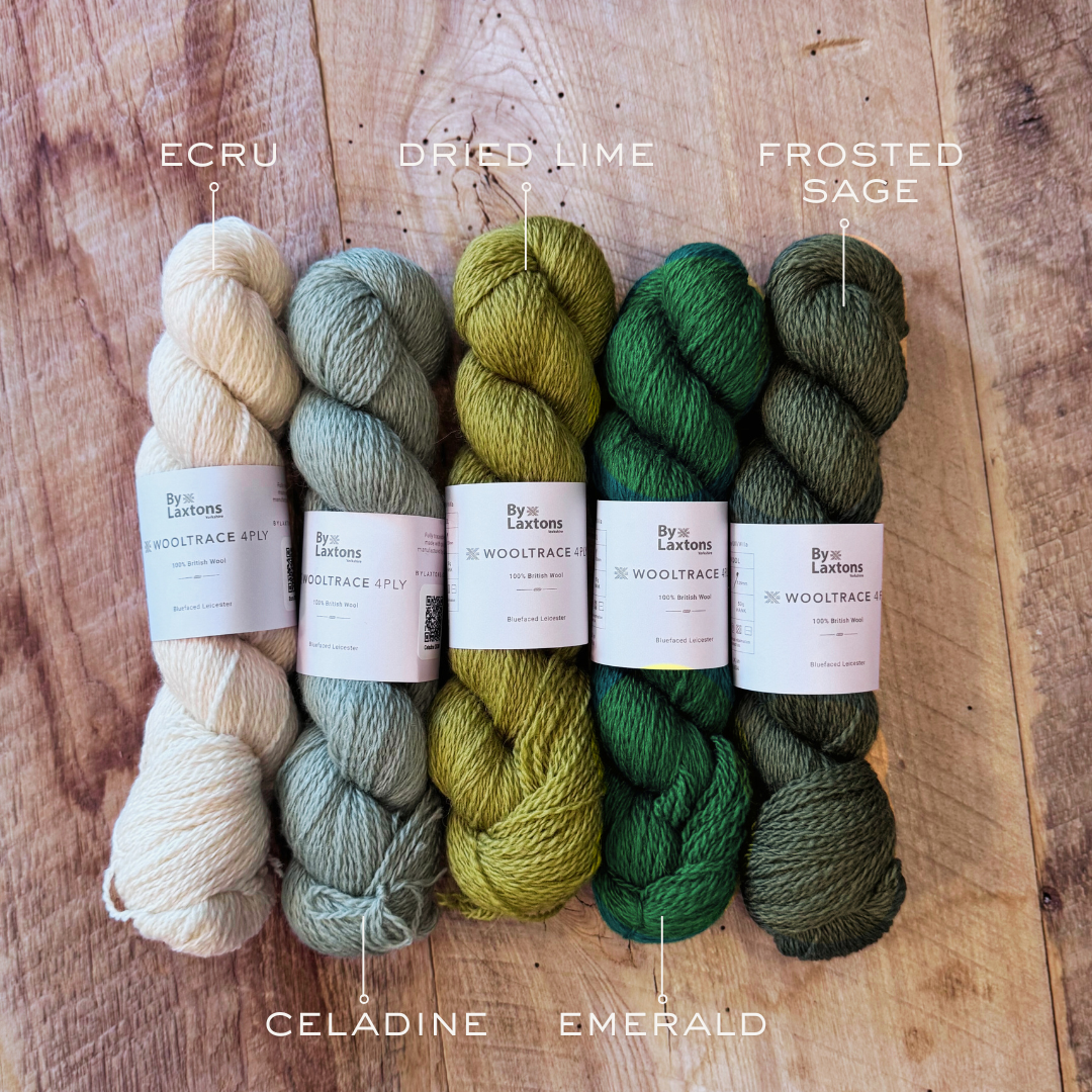 Five skeins of yarn in different shades of greens with labels on a wooden surface