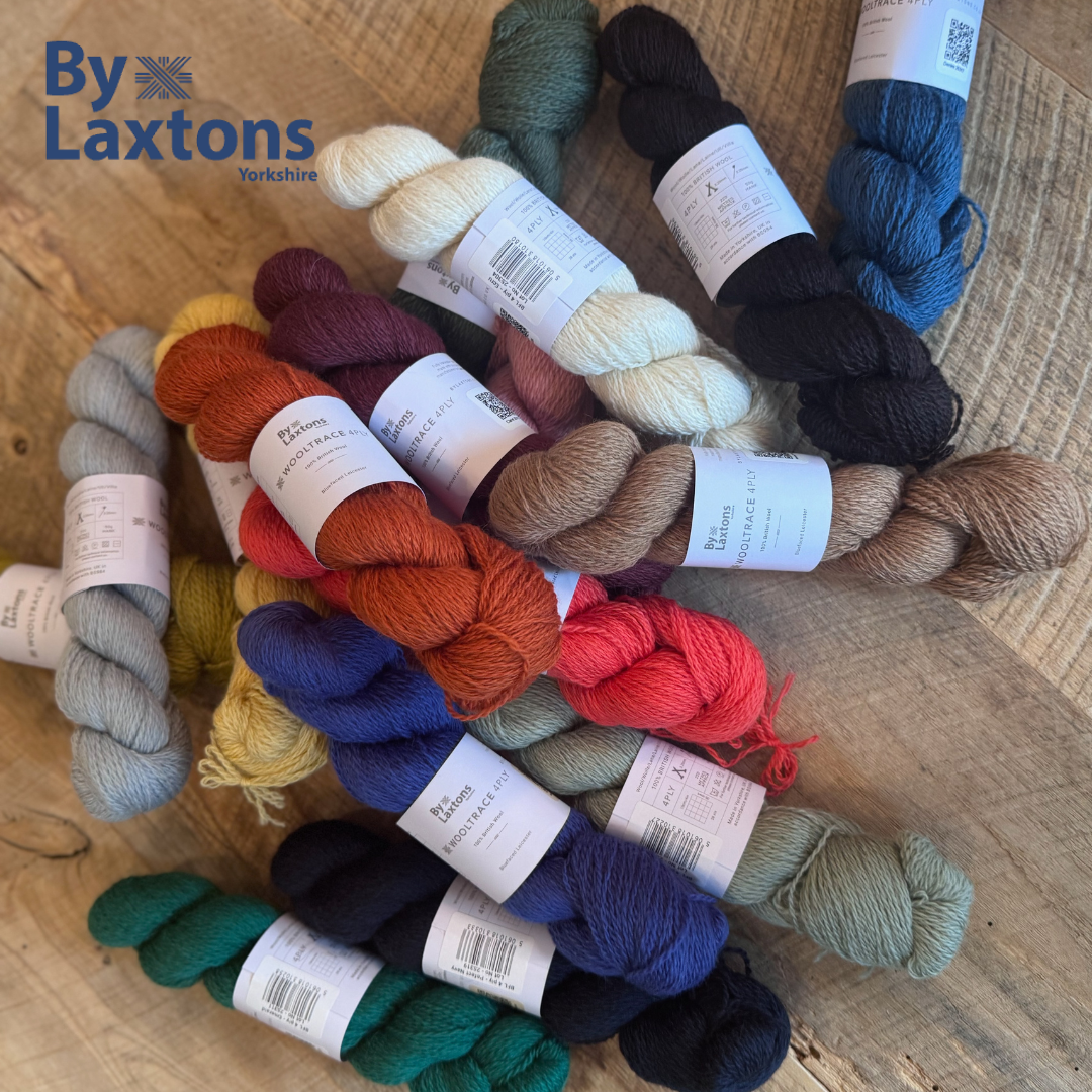 Assorted skeins of yarn in various colors with By Laxton's branding on a wooden surface.