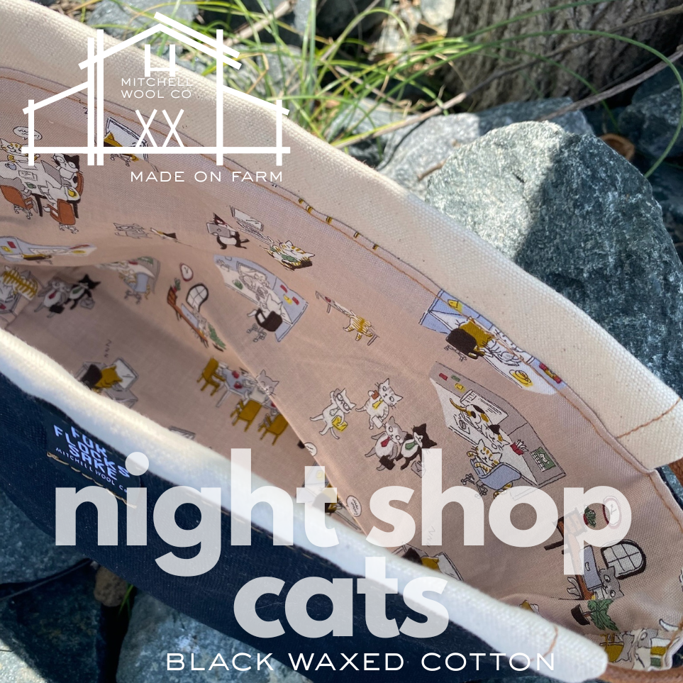 Black waxed cotton fabric with 'night shop cats' design on a rock surface, featuring Mitchell's Wool Co branding.