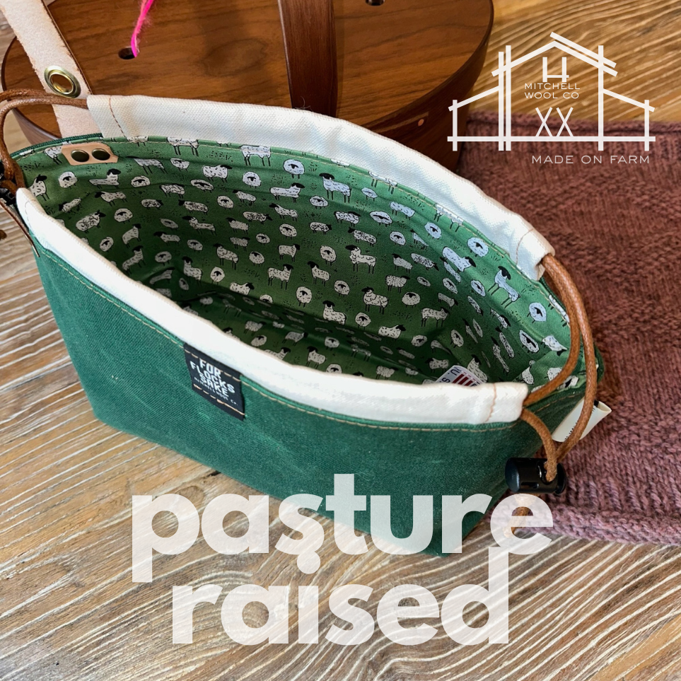 Green waxed cotton project pouch with sheep patterned lining on a wooden floor, featuring 'Mitchell Woodworks' branding.