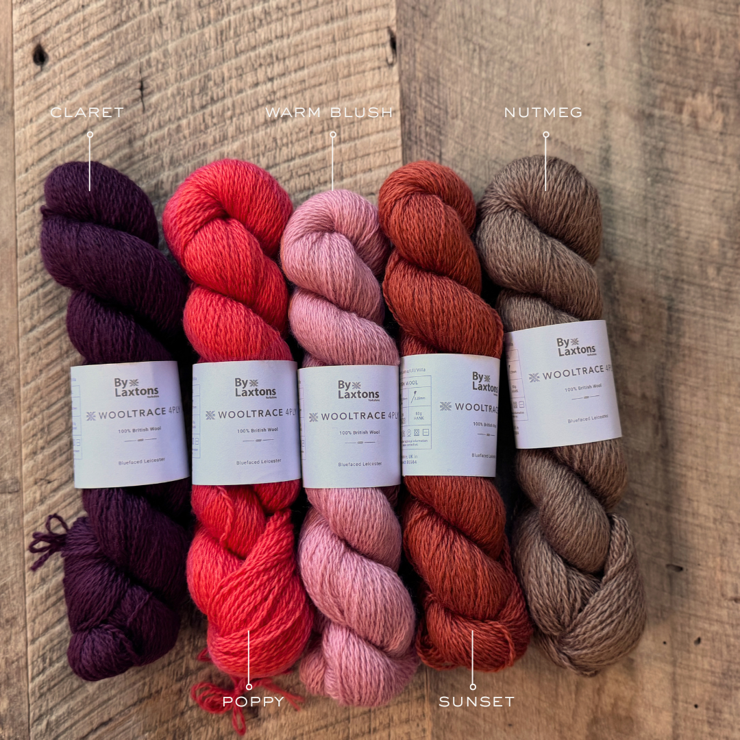 Five shades of red hued yarns - L to R CLARET, POPPY, WARM BLUSH, SUNSET, & NUTMEG bearing the Laxtons band on an old wood floor