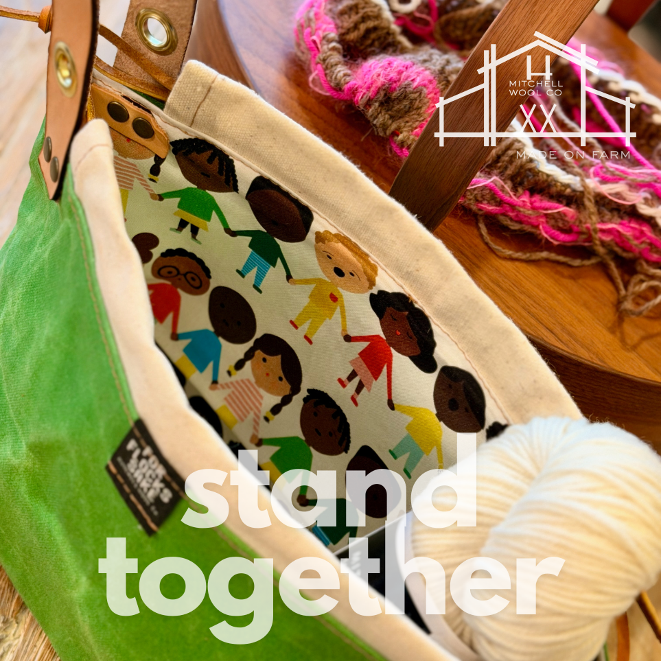 Project bag with 'stand together' text and diverse people design, placed on a wooden surface with yarn.