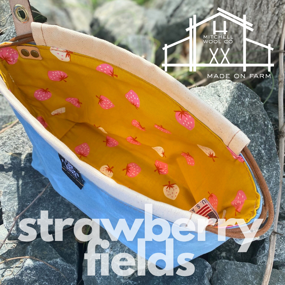 cornflower blue waxed cotton project bag with strawberry pattern on a stone surface, featuring Mitchell Wool Co branding.