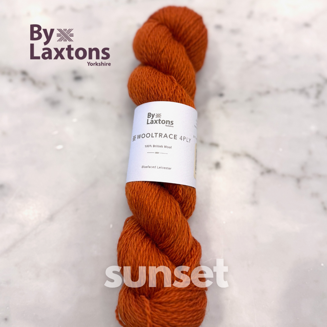 Orange skein of yarn with a By Laxton's label on a light marble background
