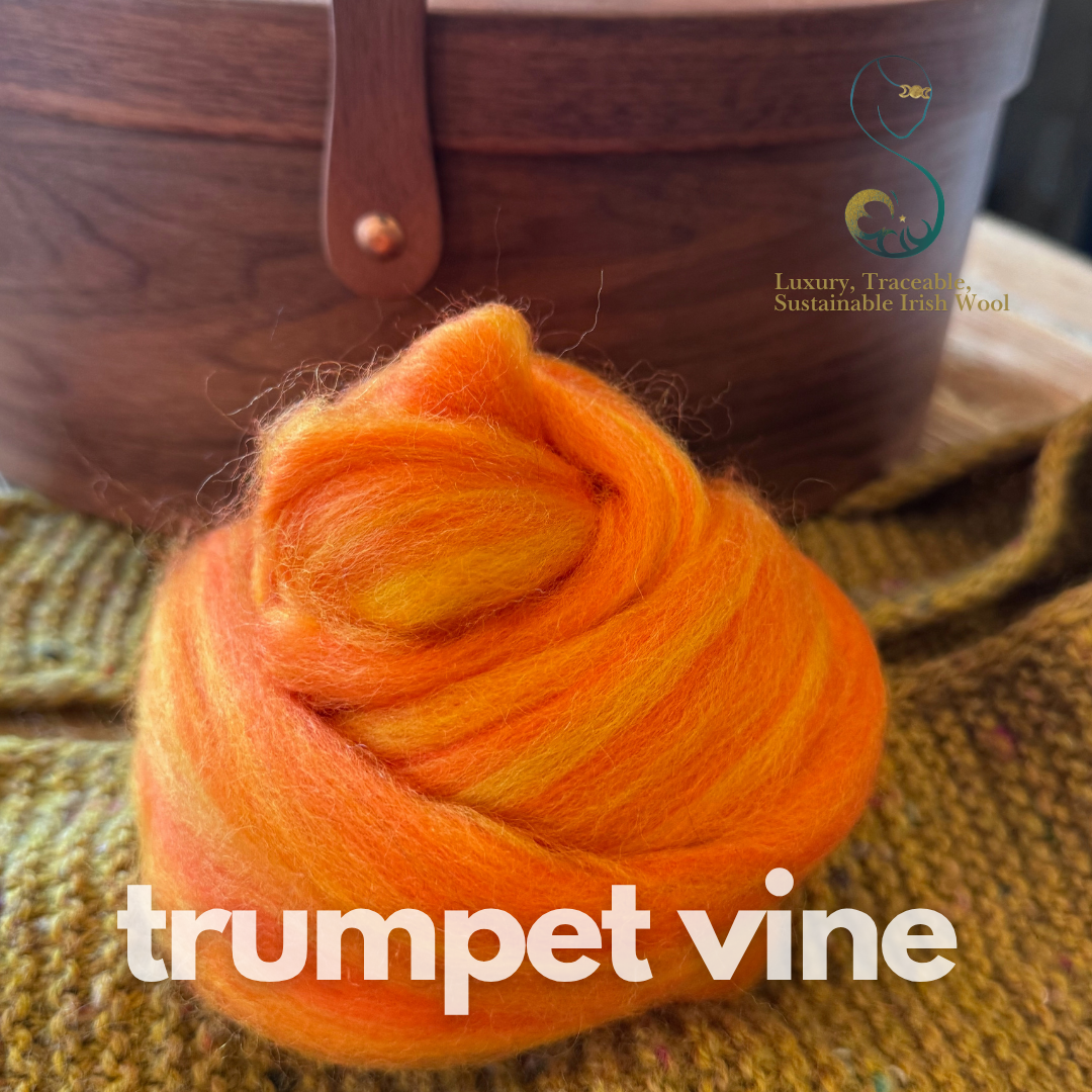 Orangedollup of combed top from BFL Irish sheep labeled 'trumpet vine' on a textured surface with a wooden basket in the background.
