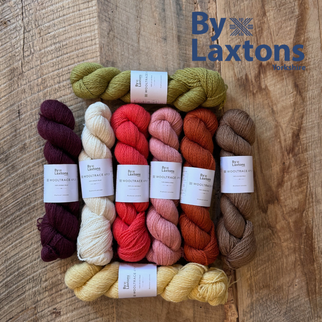 Assorted skeins of yarn on a wooden surface with By Laxtons branding.